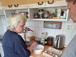P. Limberková stojí u kuchyňské linky a do misky rozklepává vejce, připravuje těsto na palačinky. Vedle ní je plato s vejci a na lince běžné kuchyňské pomůcky. Napravo stojí p. Limberk
