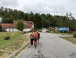 Na fotografii zachyceni zleva: p. Špinarová, DiS., p. Spáčil, p. Blechová, p. Vondra. Všichni jdou směrem k hotelovému areálu. Po stranách jsou stromy, keře a nízké budovy s červenými střechami. U vjezdu je cedule „Restaurace a Hotel“