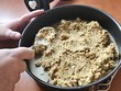 V kulaté formě je směs z ovesných vloček, která se právě připravuje. Ruce p. Fialové lžící urovnávají její povrch. Na stole vedle formy leží kuchyňské náčiní a v pozadí jsou další drobnosti