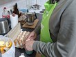 Na fotografii je zachycen p. Šopa, který v kuchyni připravuje likér. Manipuluje s vejci v papírovém obalu a vedle něj jsou na lince kuchyňské potřeby a potraviny. V pozadí je sporák s hrncem
